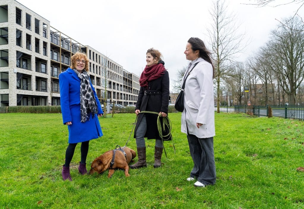 wethouder staat in blauwe jas links, in het midden staat een inwoner met bruine hond en gebiedsregisseur in witte jas aan de rechterkant. 