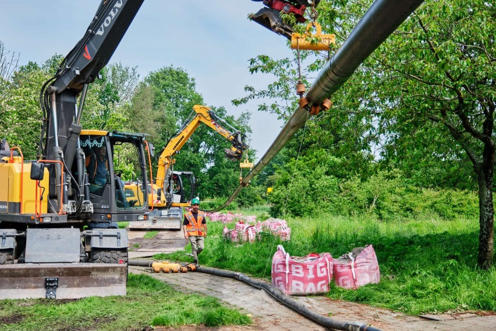 Meerdere hijskranen hijsen leidingen voor het warmtenet omhoog.