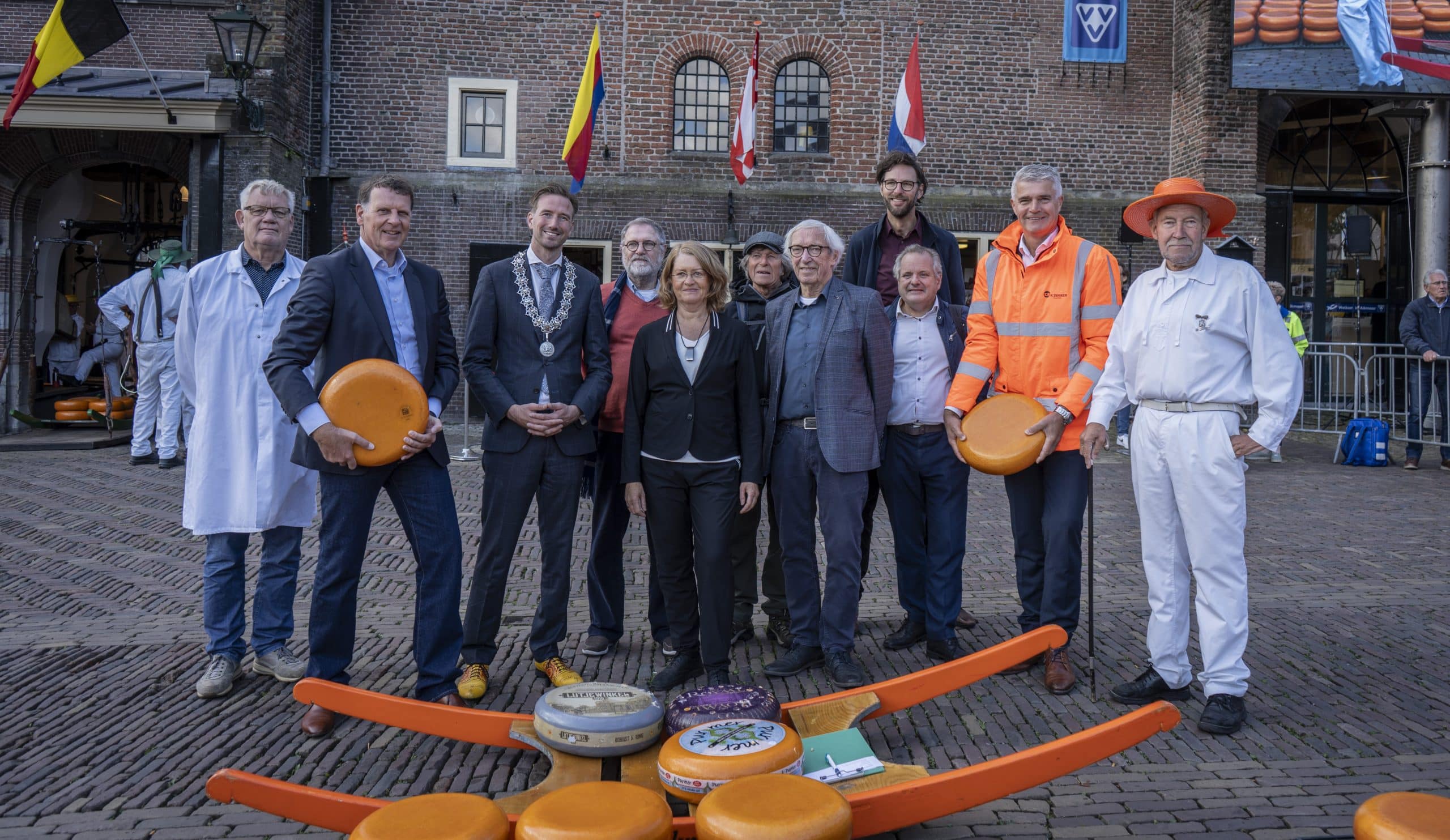 Wethouder Christian Schouten en andere betrokkenen bij het Energieleverend Geluidsscherm staan op het Waagplein voor een traditionele kaasberrie met kazen.