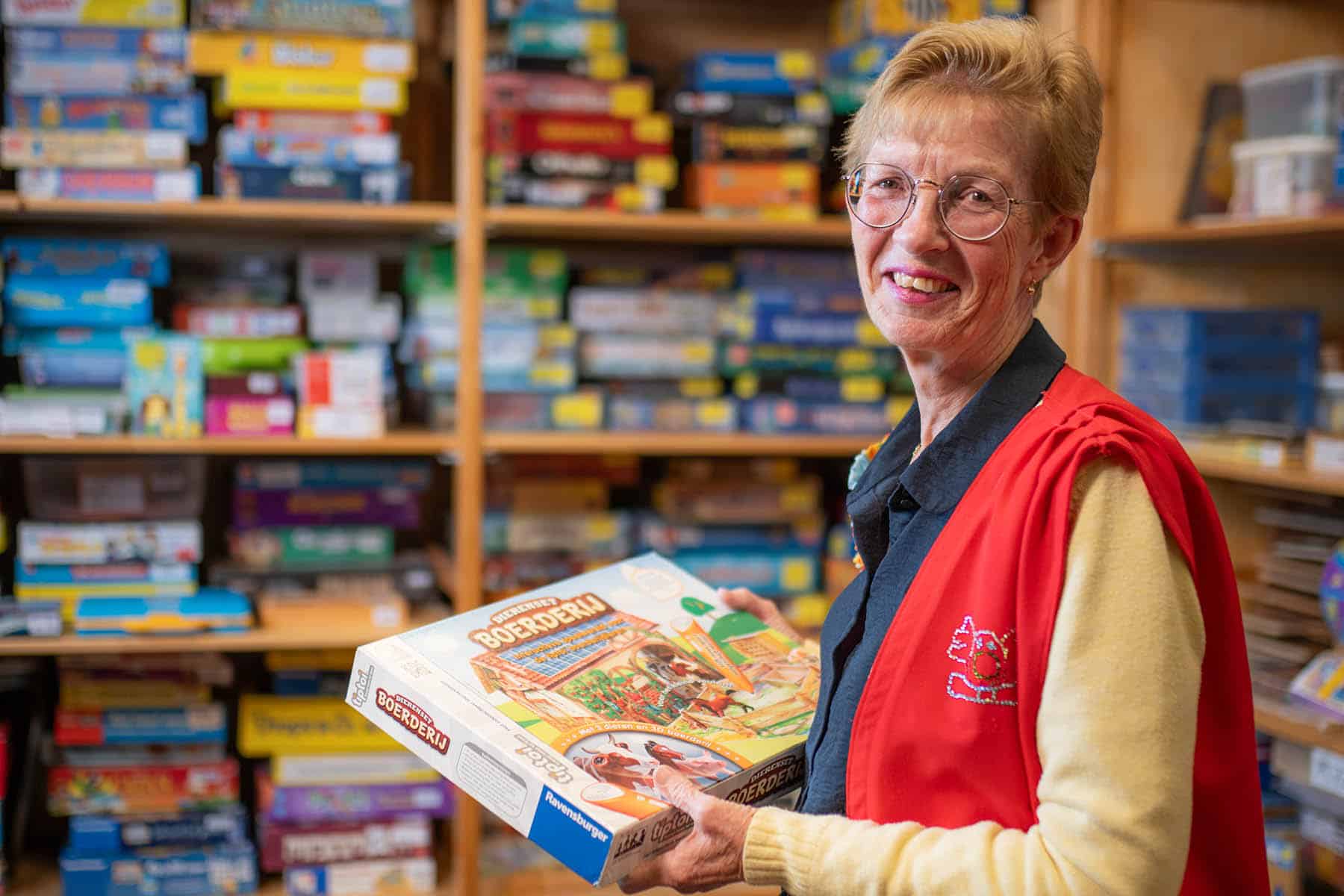 Vrouw houdt een spel vast. Op de achtergrond de spellenkast van de speel-o-theek.